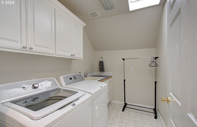 clothes washing area featuring washing machine and clothes dryer, a skylight, sink, and cabinets