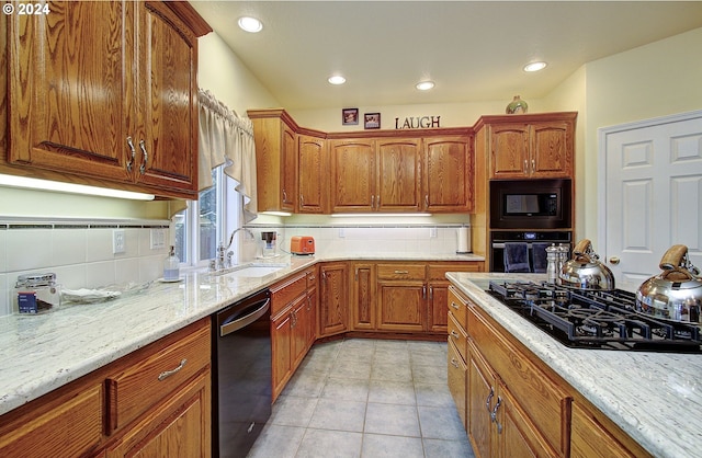 kitchen featuring tasteful backsplash, light stone countertops, sink, and black appliances