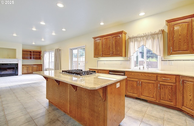 kitchen featuring a kitchen breakfast bar, light stone counters, stainless steel gas cooktop, a fireplace, and a kitchen island