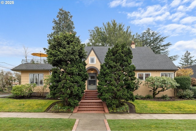 view of front of house with stucco siding, a shingled roof, and a front lawn