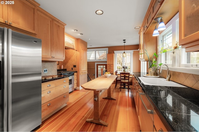 kitchen featuring pendant lighting, light wood-style flooring, a sink, appliances with stainless steel finishes, and decorative backsplash