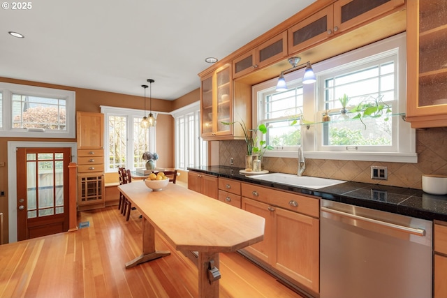 kitchen with backsplash, glass insert cabinets, light wood-style flooring, stainless steel dishwasher, and a sink