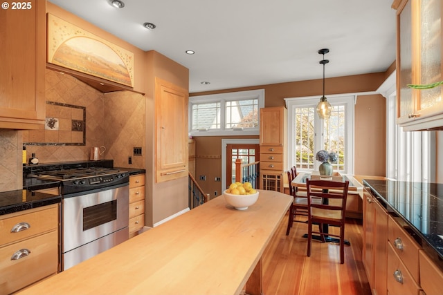 kitchen featuring stainless steel gas stove, glass insert cabinets, tile countertops, light wood-style floors, and decorative backsplash