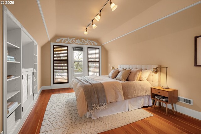 bedroom featuring vaulted ceiling, rail lighting, baseboards, and hardwood / wood-style floors