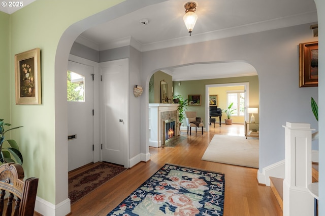 entryway with light wood-type flooring, arched walkways, crown molding, and a tile fireplace