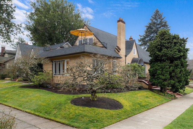 view of side of home featuring a yard, stone siding, a chimney, and a balcony