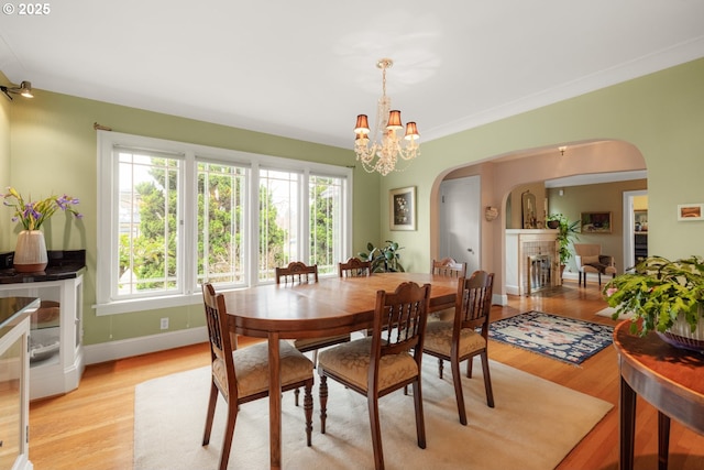 dining space with arched walkways, a notable chandelier, a fireplace, and light wood-type flooring