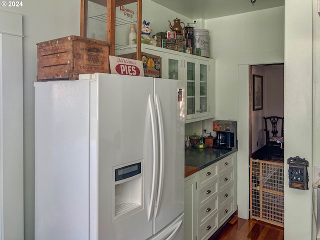 kitchen with white refrigerator with ice dispenser, dark wood finished floors, dark countertops, glass insert cabinets, and white cabinets