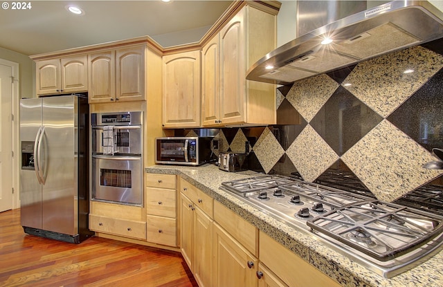 kitchen featuring light brown cabinets, stainless steel appliances, wall chimney range hood, and hardwood / wood-style flooring