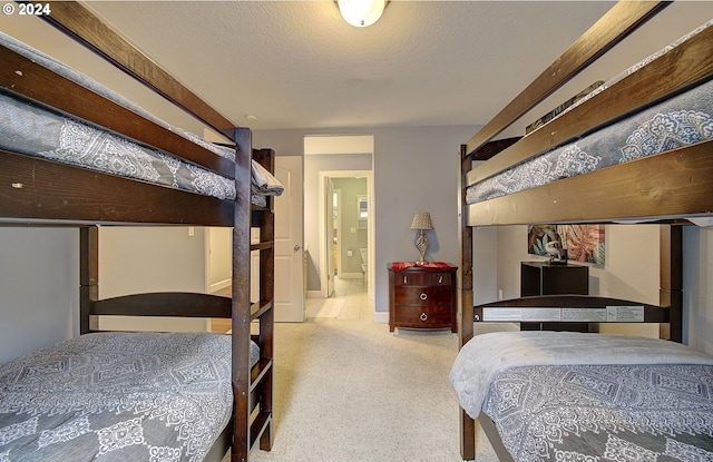 bedroom with light carpet, ensuite bathroom, and a textured ceiling