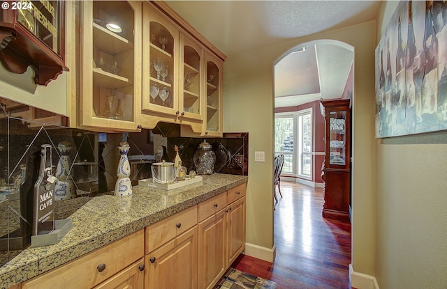 bar with a textured ceiling, decorative backsplash, and dark wood-type flooring