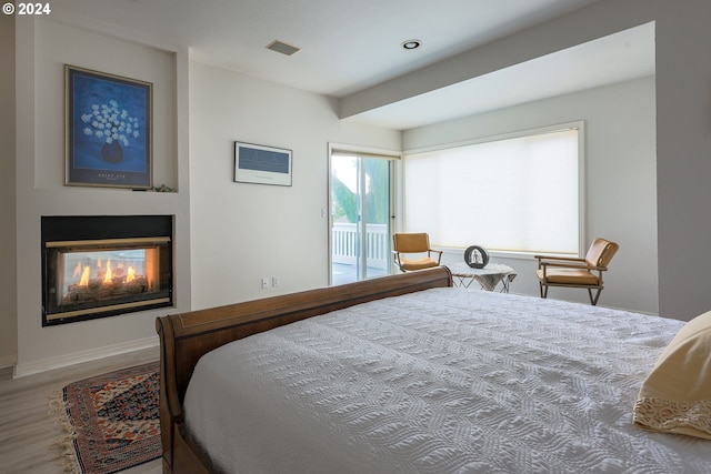 bedroom featuring wood finished floors, visible vents, a multi sided fireplace, and access to exterior