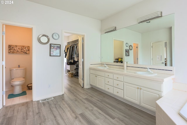 bathroom featuring wood finished floors, visible vents, double vanity, a sink, and toilet