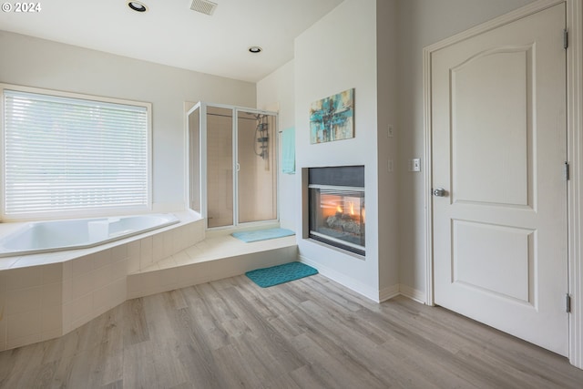 bathroom featuring visible vents, a garden tub, a stall shower, wood finished floors, and a glass covered fireplace