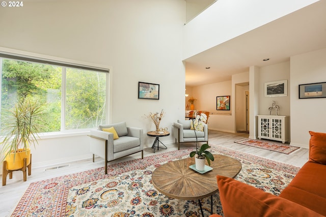 living area with wood finished floors, visible vents, a towering ceiling, and baseboards