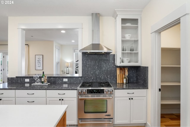 kitchen with dark stone countertops, white cabinetry, high end stainless steel range, and wall chimney range hood