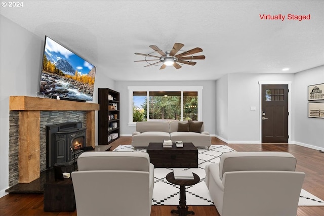 living room with wood-type flooring, a textured ceiling, a wood stove, and ceiling fan