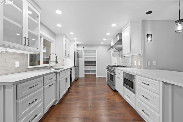 kitchen featuring appliances with stainless steel finishes, sink, wall chimney range hood, a barn door, and white cabinets