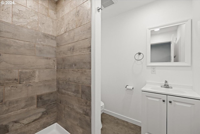 bathroom with a tile shower, vanity, and toilet