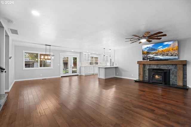 unfurnished living room featuring ceiling fan, a stone fireplace, dark hardwood / wood-style flooring, and a textured ceiling