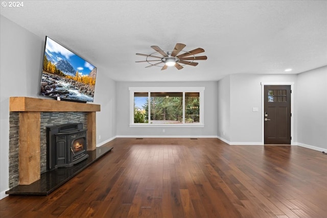 unfurnished living room featuring dark hardwood / wood-style floors, ceiling fan, a wood stove, and a textured ceiling