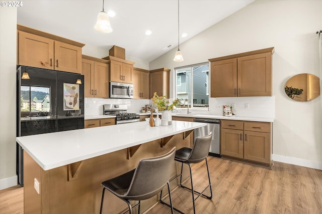 kitchen featuring a breakfast bar, a center island, hanging light fixtures, vaulted ceiling, and stainless steel appliances