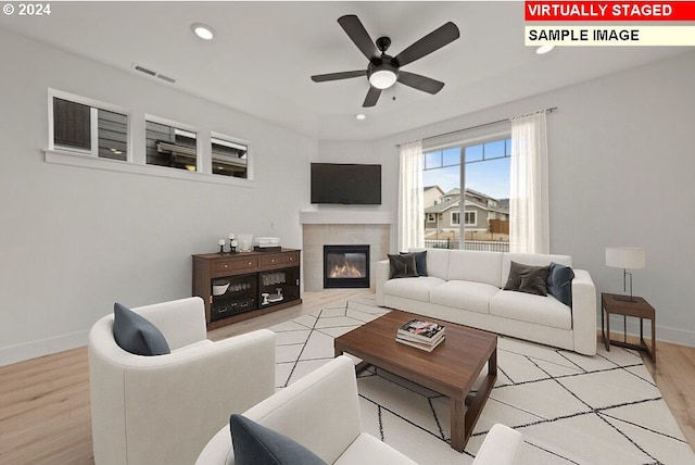 living room with light wood-type flooring, ceiling fan, and a tile fireplace