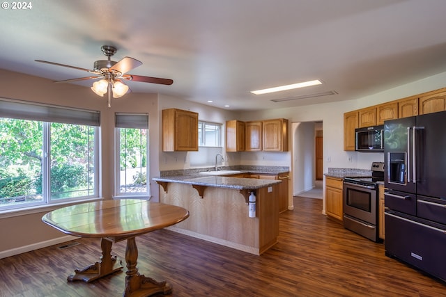 kitchen featuring light stone countertops, black appliances, sink, dark wood-type flooring, and a breakfast bar area