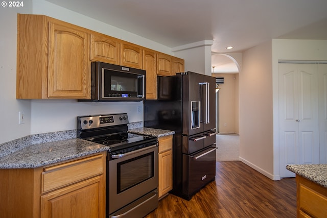 kitchen with appliances with stainless steel finishes, dark wood-type flooring, and dark stone counters