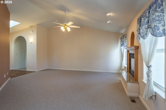 unfurnished living room with vaulted ceiling with skylight, light carpet, and ceiling fan