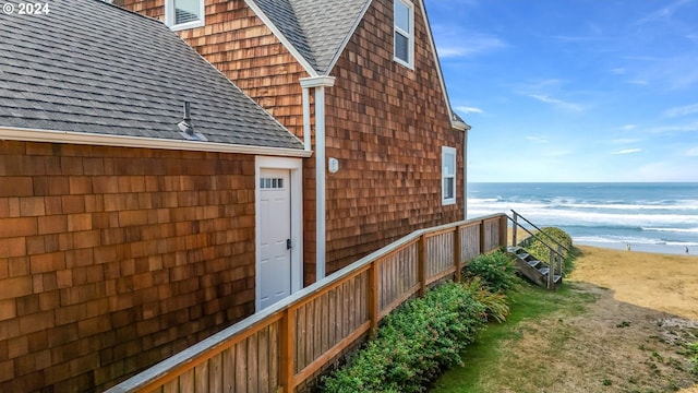 view of side of property with a beach view, a water view, and roof with shingles