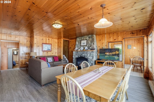 dining room with a stone fireplace, wood finished floors, wooden walls, and wooden ceiling
