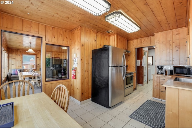 kitchen featuring light brown cabinetry, light tile patterned floors, stainless steel appliances, wood walls, and pendant lighting