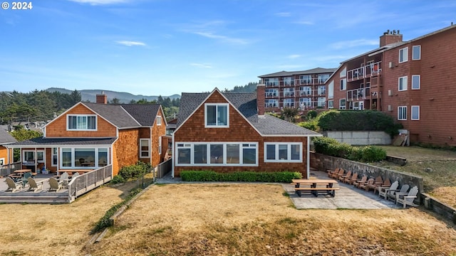 rear view of house featuring a shingled roof, a mountain view, a chimney, a patio area, and a lawn