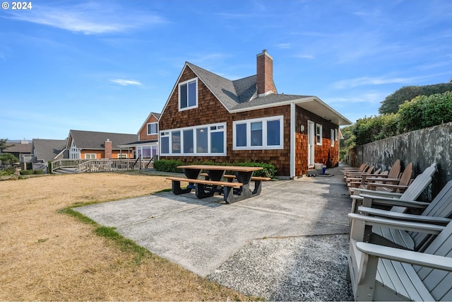 rear view of house featuring fence, roof with shingles, a chimney, a patio area, and a yard