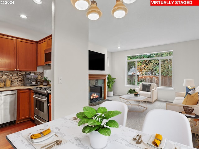 kitchen with hardwood / wood-style floors, a premium fireplace, decorative backsplash, and appliances with stainless steel finishes