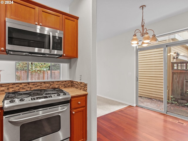 kitchen with hanging light fixtures, appliances with stainless steel finishes, wood-type flooring, and an inviting chandelier