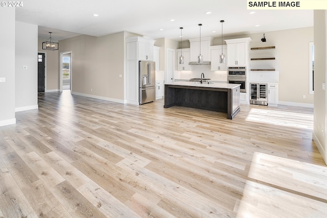 kitchen featuring decorative light fixtures, appliances with stainless steel finishes, light hardwood / wood-style floors, wine cooler, and an island with sink