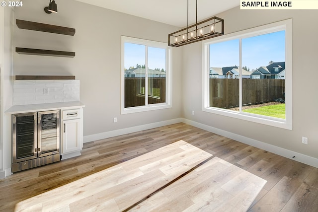 unfurnished living room featuring wine cooler, a notable chandelier, and light hardwood / wood-style floors