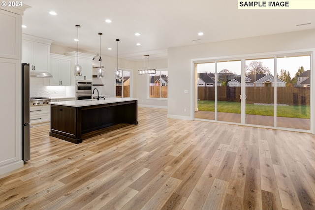 kitchen featuring pendant lighting, an inviting chandelier, a center island with sink, light hardwood / wood-style flooring, and sink