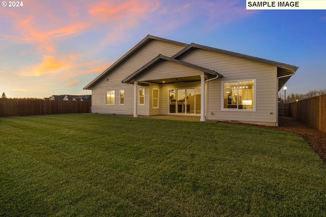 back house at dusk featuring ceiling fan and a lawn