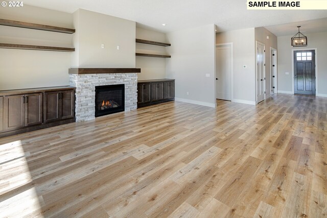 unfurnished living room featuring an inviting chandelier, a stone fireplace, and light wood-type flooring