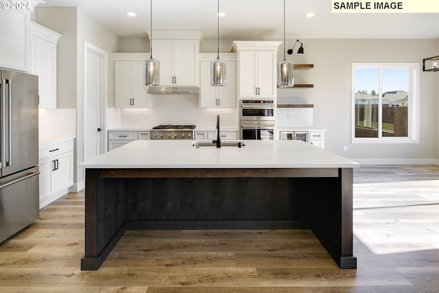 kitchen featuring appliances with stainless steel finishes, sink, light wood-type flooring, a kitchen island with sink, and hanging light fixtures