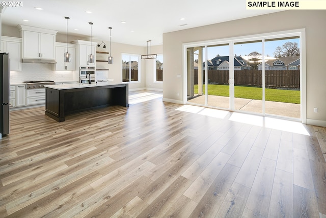 kitchen with an island with sink, pendant lighting, light hardwood / wood-style floors, tasteful backsplash, and appliances with stainless steel finishes