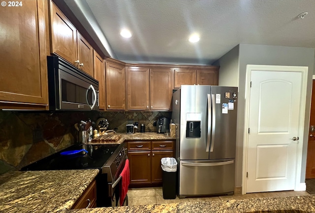 kitchen featuring appliances with stainless steel finishes, tasteful backsplash, dark stone counters, a textured ceiling, and light tile patterned floors