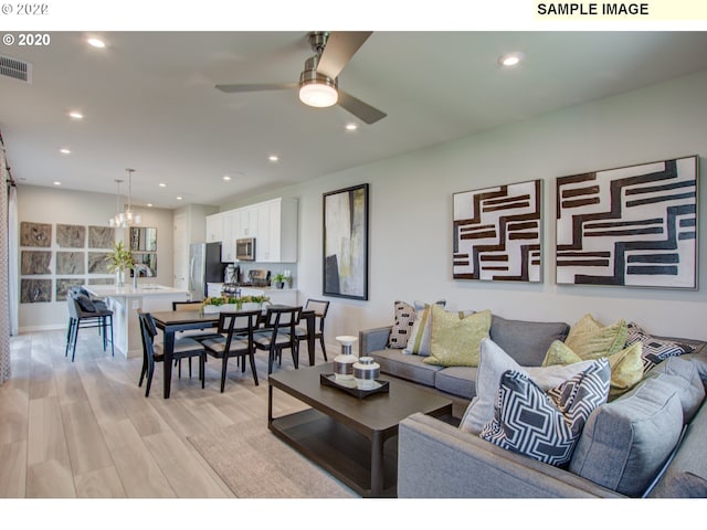 living room with ceiling fan with notable chandelier and light hardwood / wood-style floors