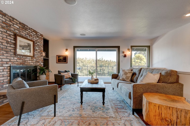 living room featuring light wood-type flooring, a textured ceiling, and a brick fireplace