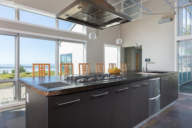 kitchen featuring a kitchen island with sink, stainless steel gas cooktop, a water view, and a towering ceiling