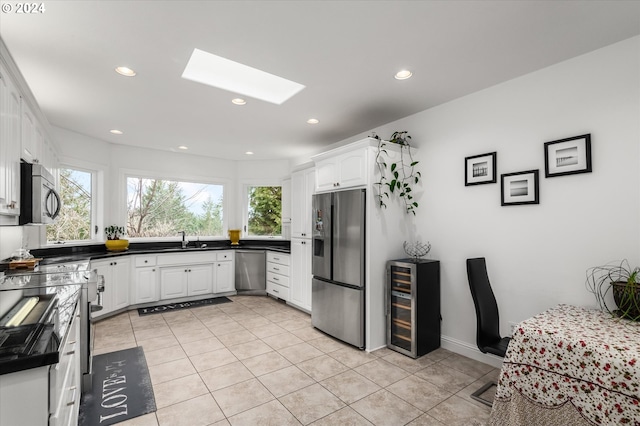 kitchen with white cabinets, wine cooler, a skylight, light tile patterned floors, and appliances with stainless steel finishes