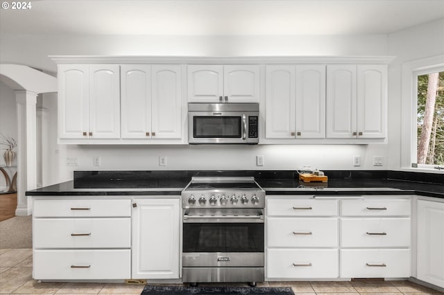 kitchen with white cabinets, dark stone countertops, light tile patterned floors, ornate columns, and appliances with stainless steel finishes